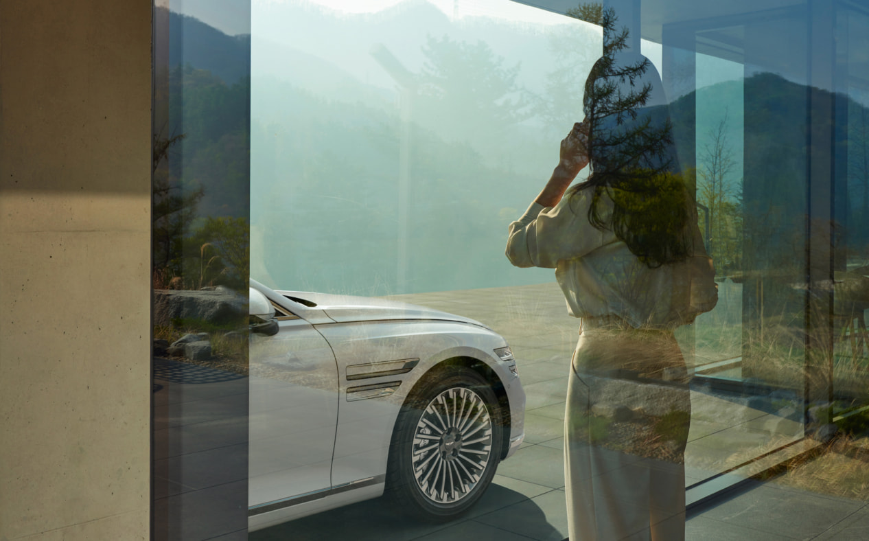 A woman talking on the phone indoors, while looking at a vehicle parked outdoors.